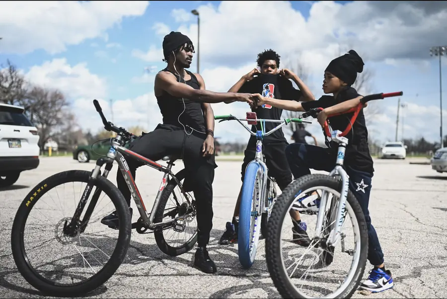 Three young riders on customized bikes in a parking lot; two of them bump fists.