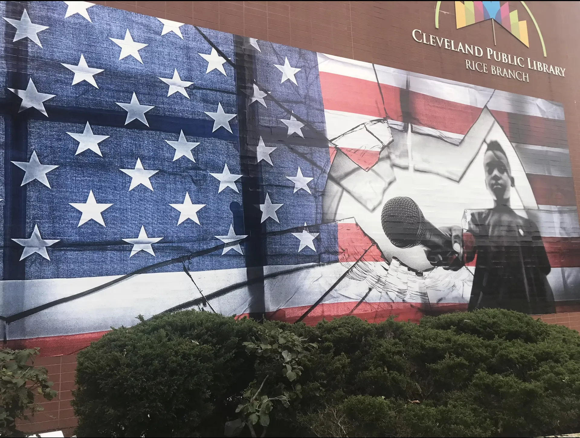 Mural of a cracked American flag, a hand holding a microphone, and a boy at a lectern, on the Cleveland Public Library Rice Branch.
