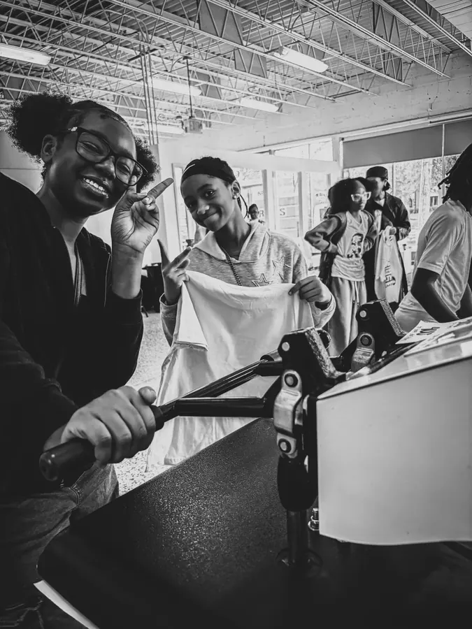 A young printer holds up the shirt she just made, grinning.